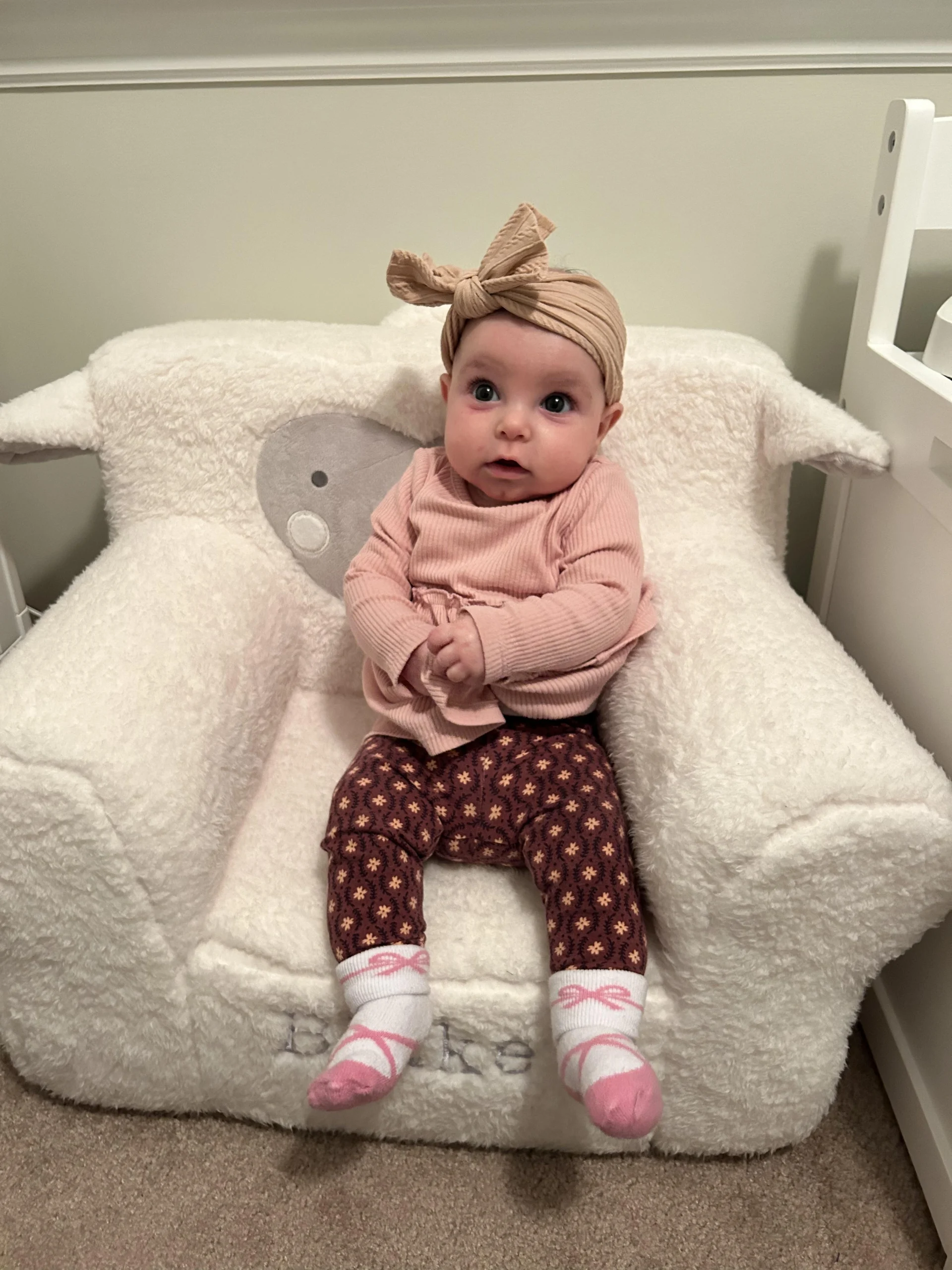 A baby wearing a bow sits in a fuzzy white chair