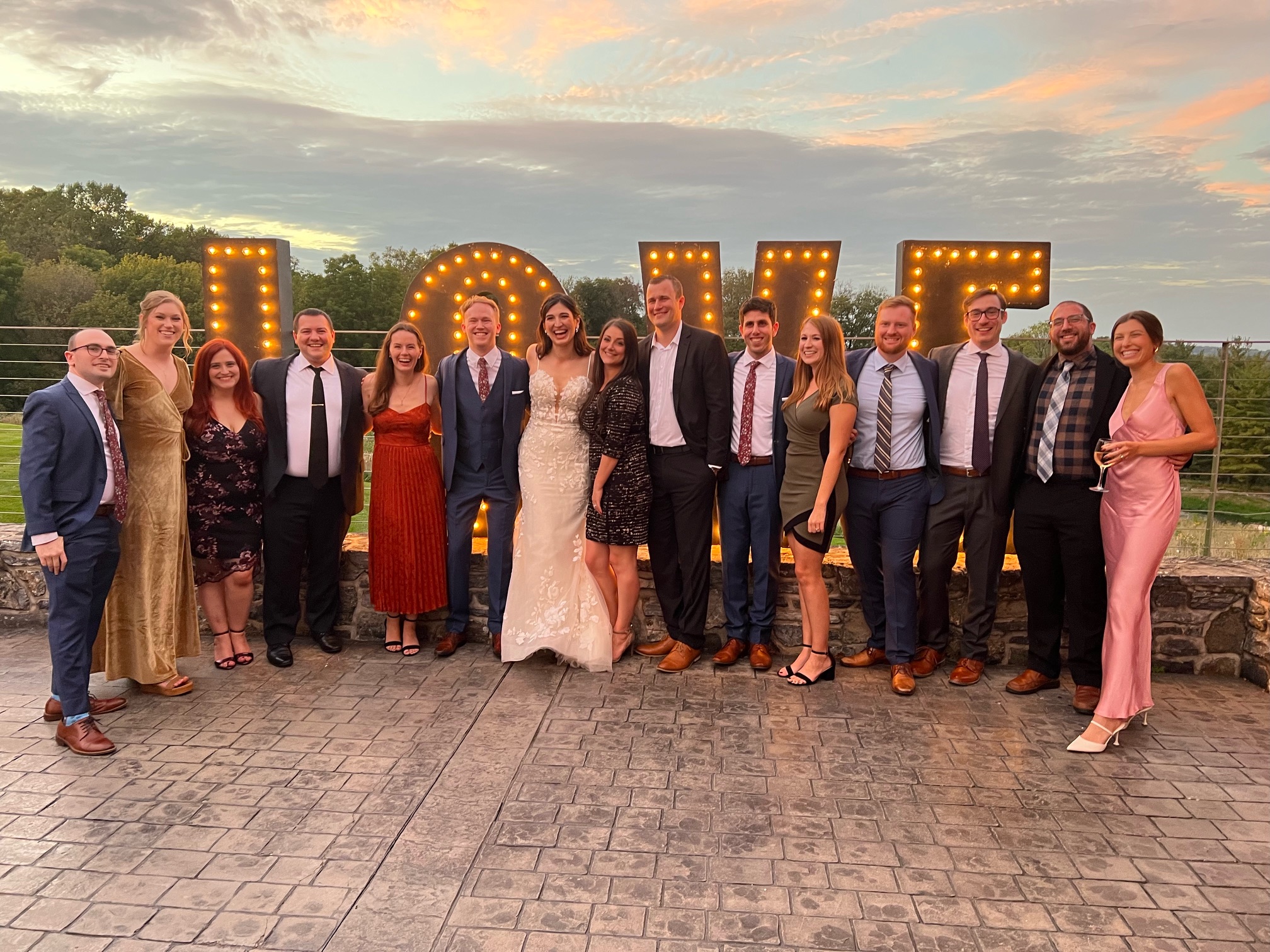 A large group of people at a wedding, including the bride and groom, pose in front of large letters that say LOVE