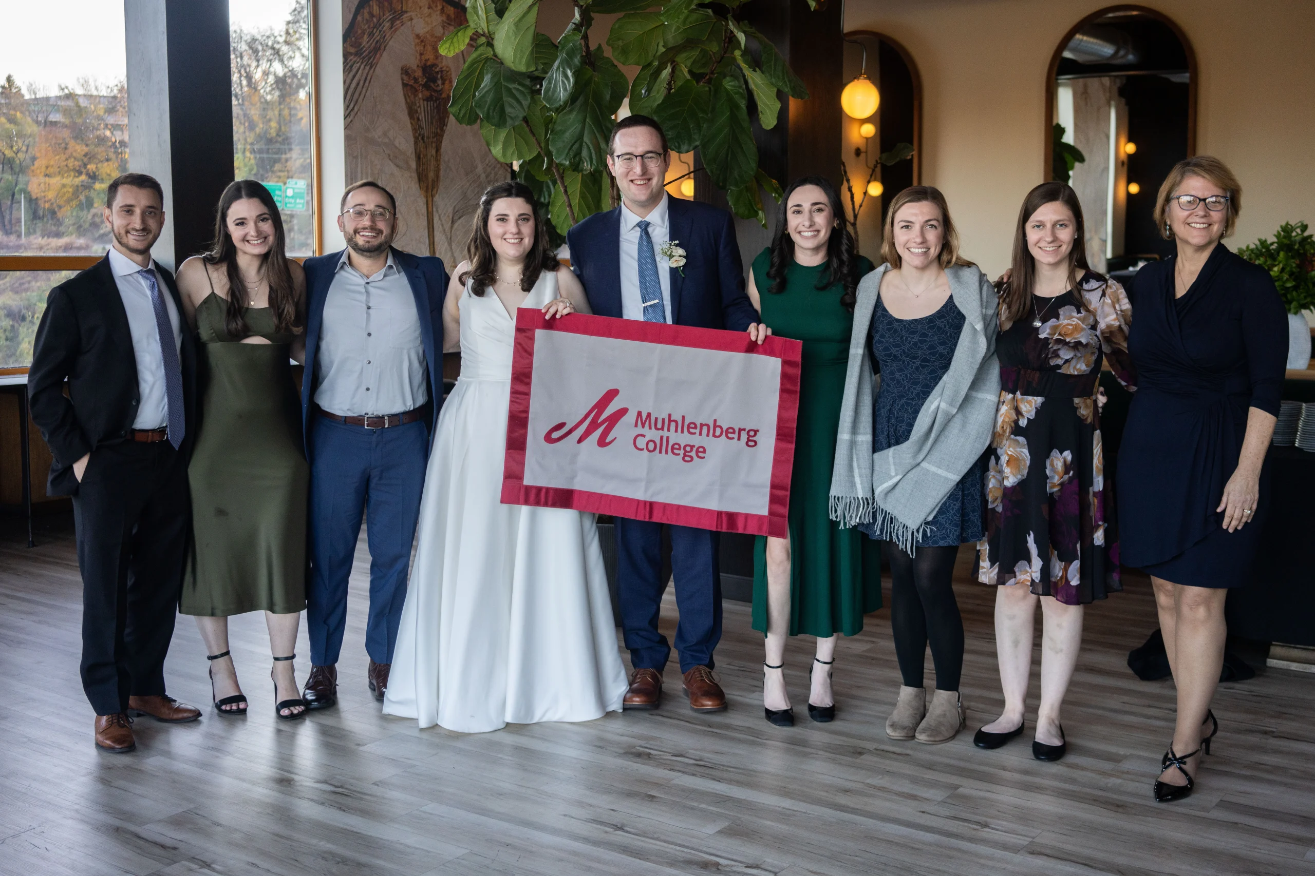 A married couple holds a flag that says Muhlenberg College and poses with friends and former professors