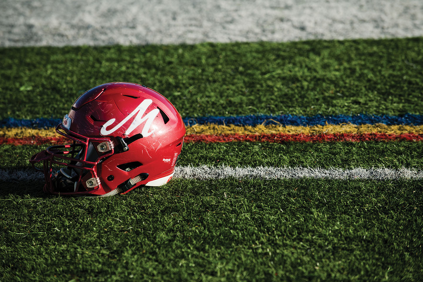 A red football helmet with a white M on it on a football field