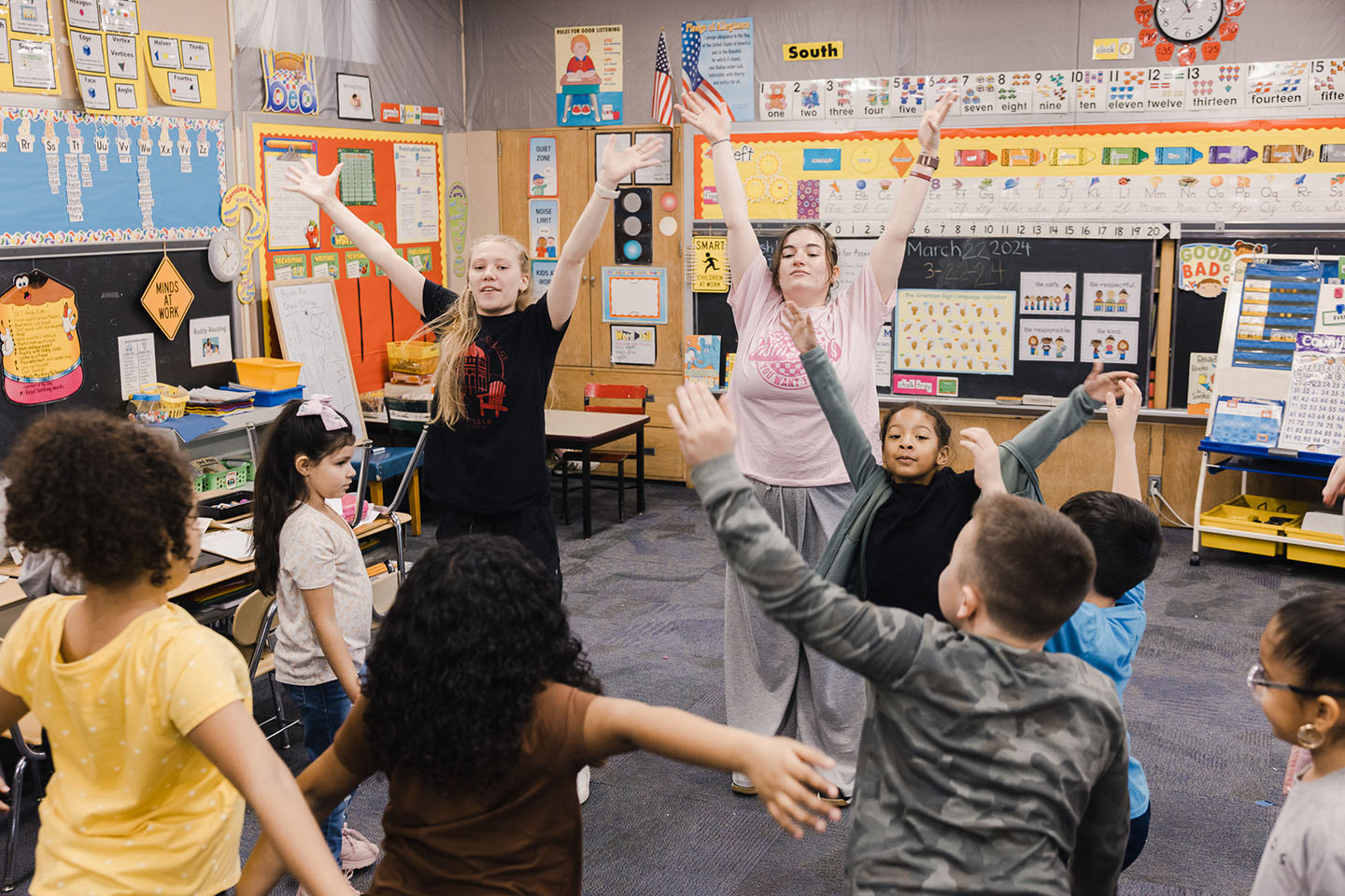 Two college students in a second grade classroom lead the kids in a dance