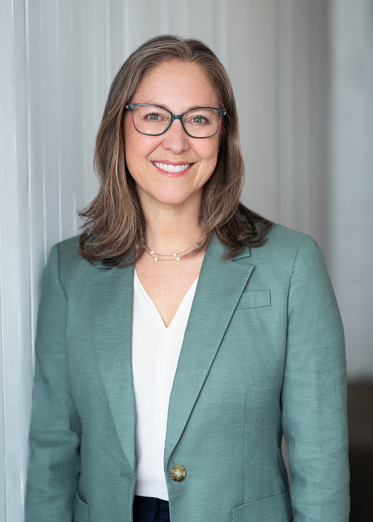 A headshot of a woman in glasses and a light blue blazer