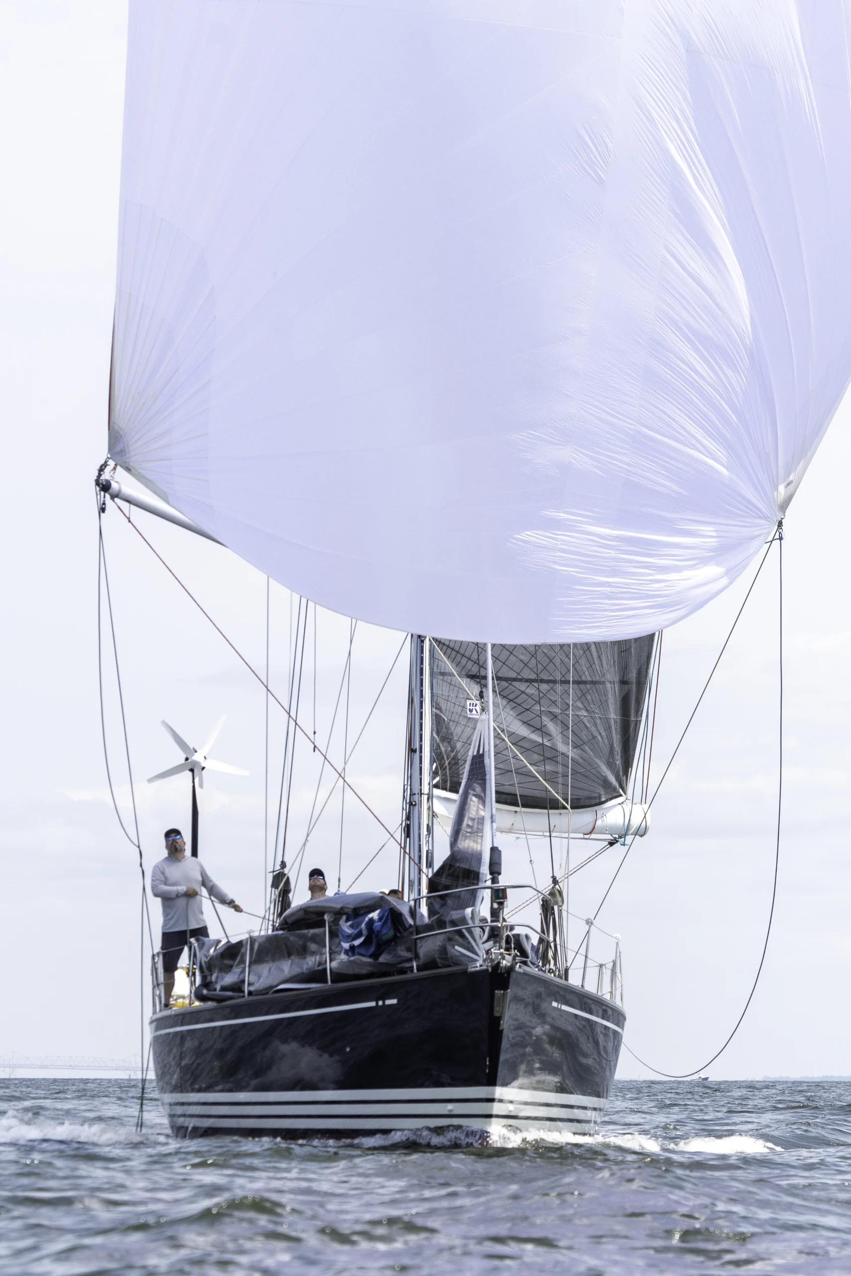 A straight on shot of a black sailboat on the ocean