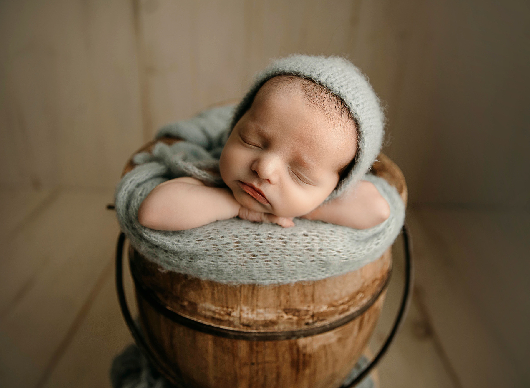 A sleeping infant in a gray hat in a bucket rests his head on his arms