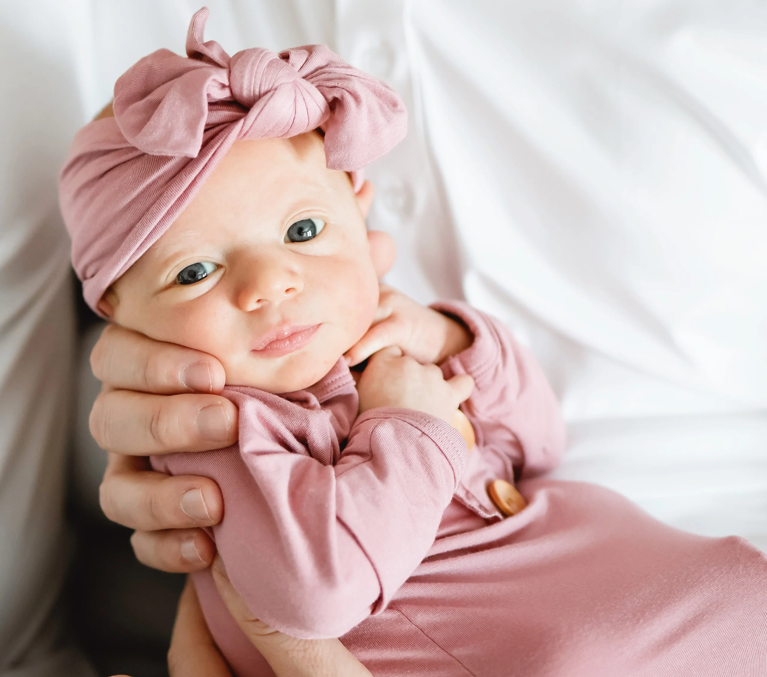 A baby with a pink bow and matching pink outfit starting at the camera