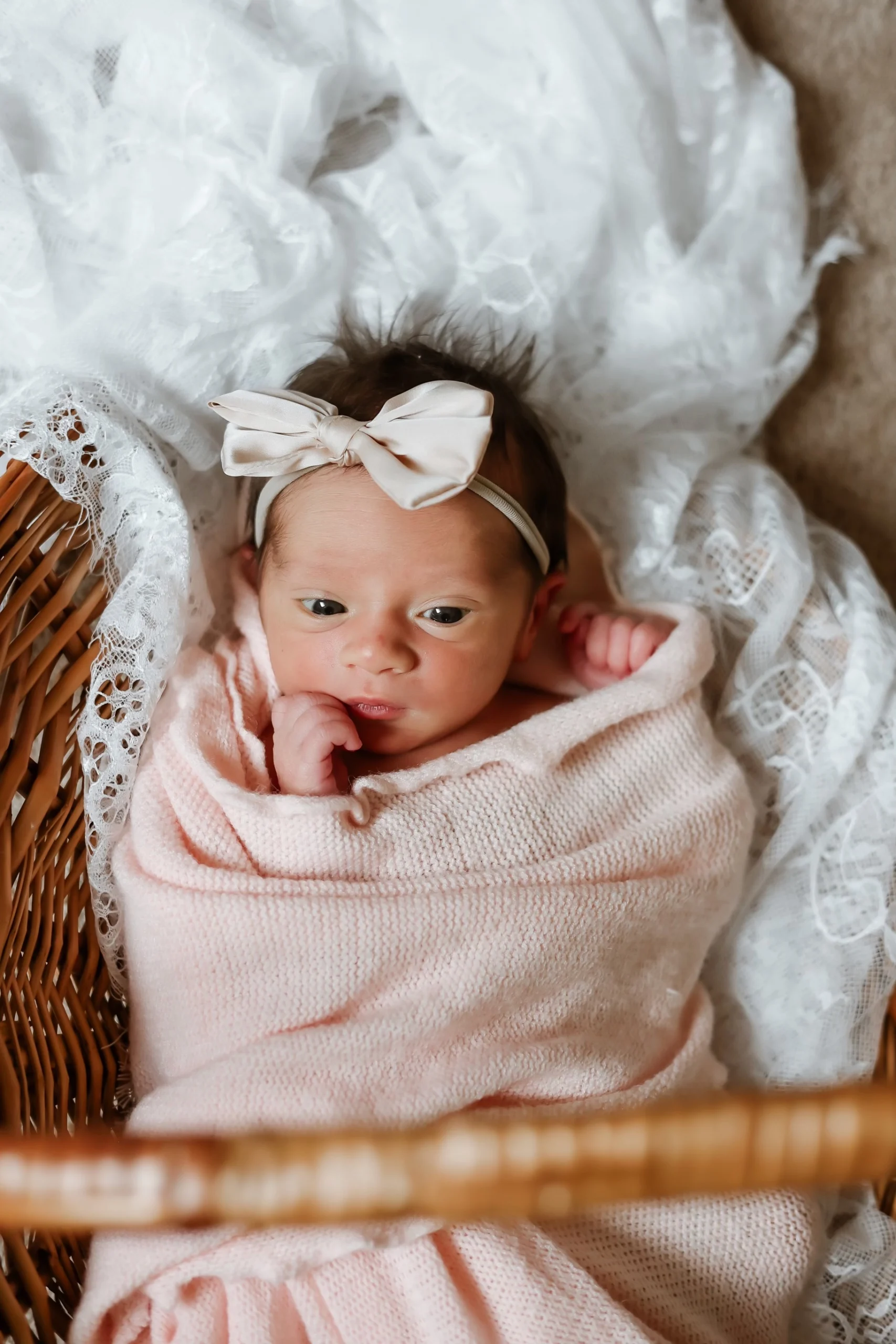 A baby with a cream bow, swaddled in a pink blanket