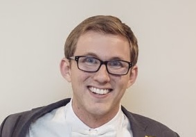 A headshot of a young man with glasses