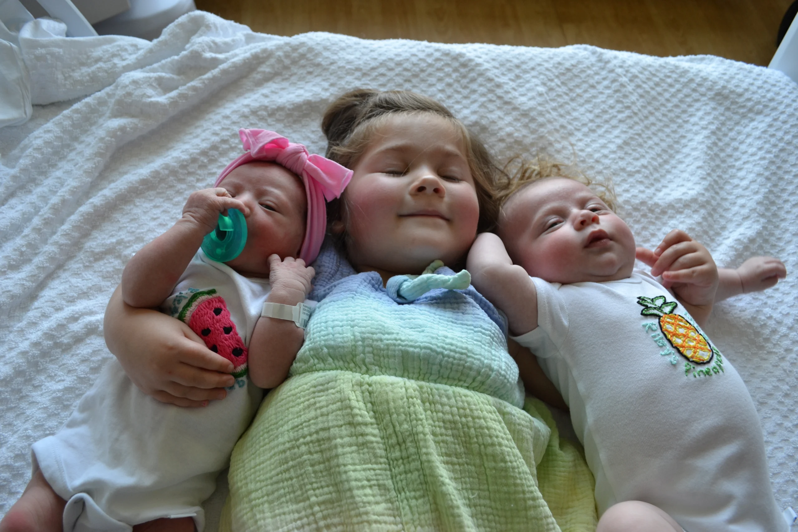 A child in the middle lays down while holding two babies on either side