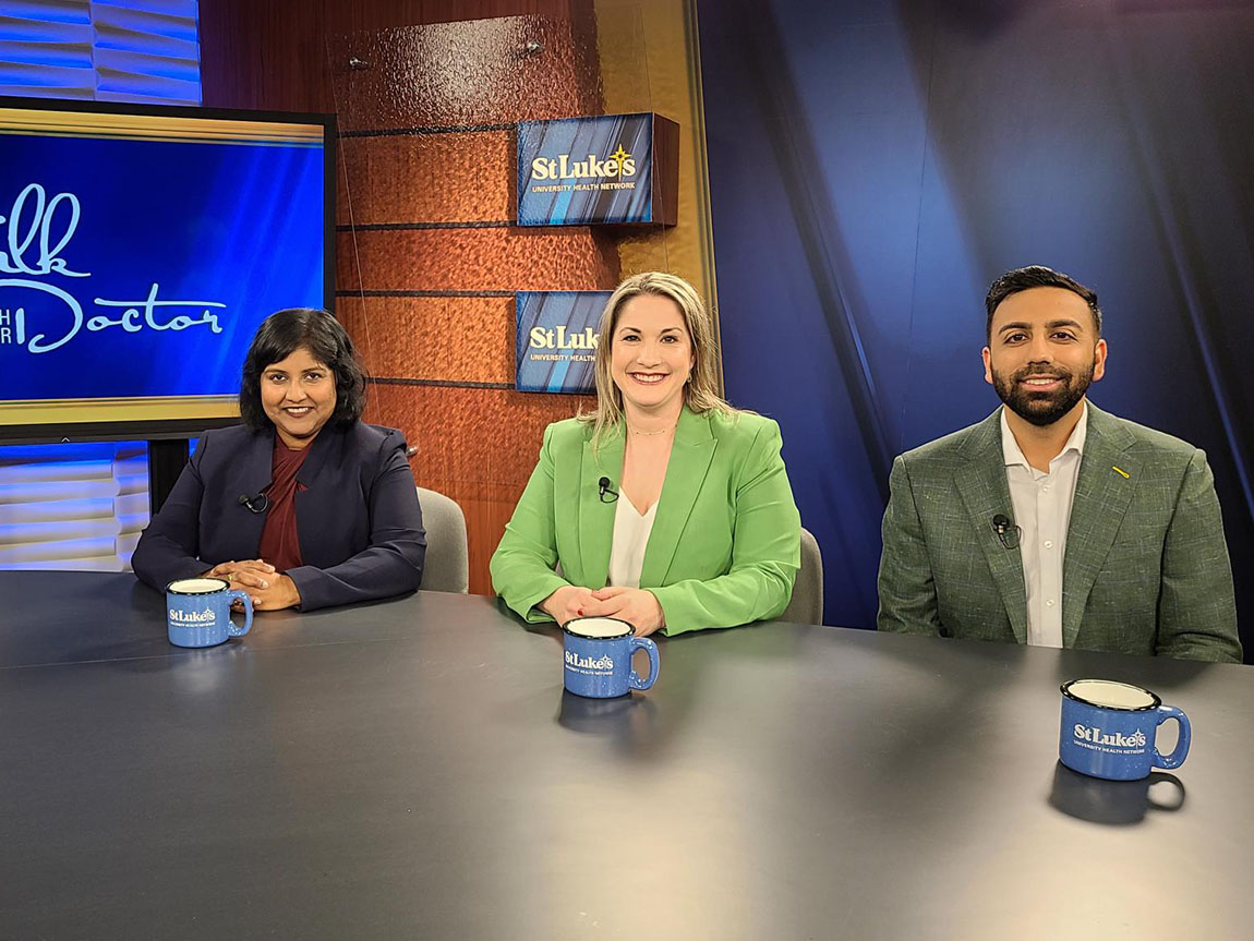 Three people smile at the camera on the set of a television talk show