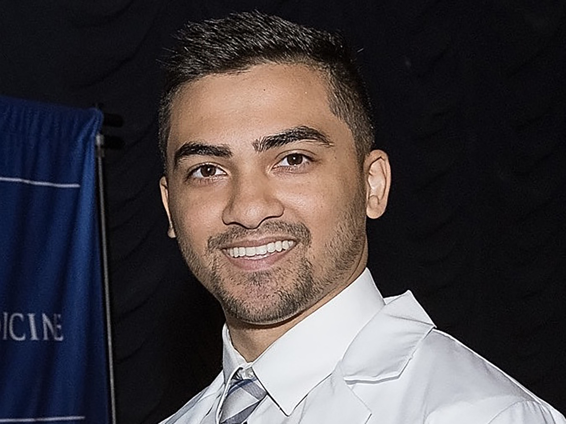 A headshot of a young adult with dark hair in a white coat