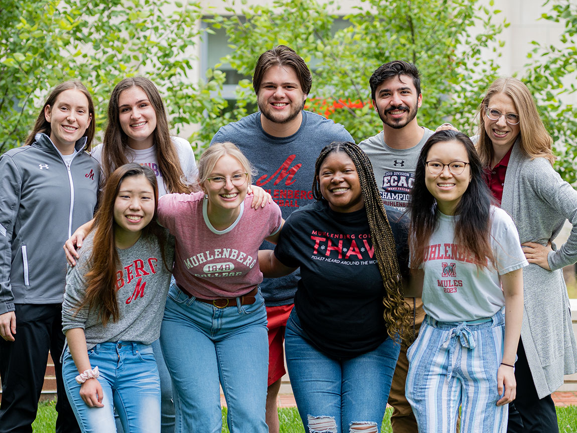 A group shot of several college students and a college professor taken outside in summer