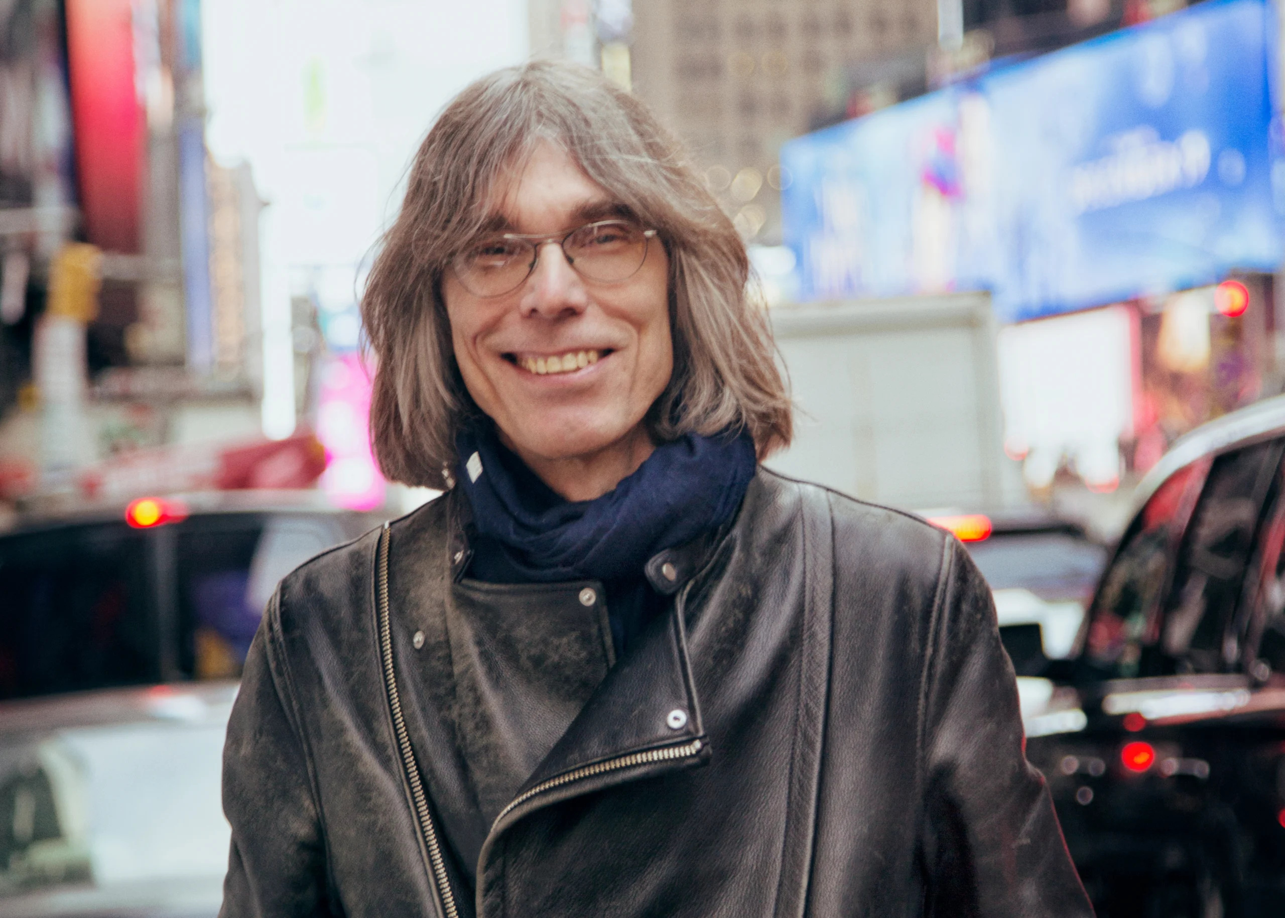 Photo of David Fricke smiling in a leather jacket with a blurred city street background