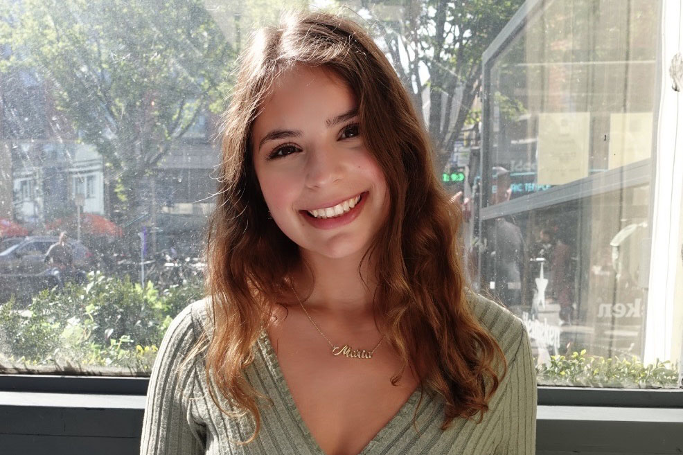 A picture of a young woman smiling in front of a window