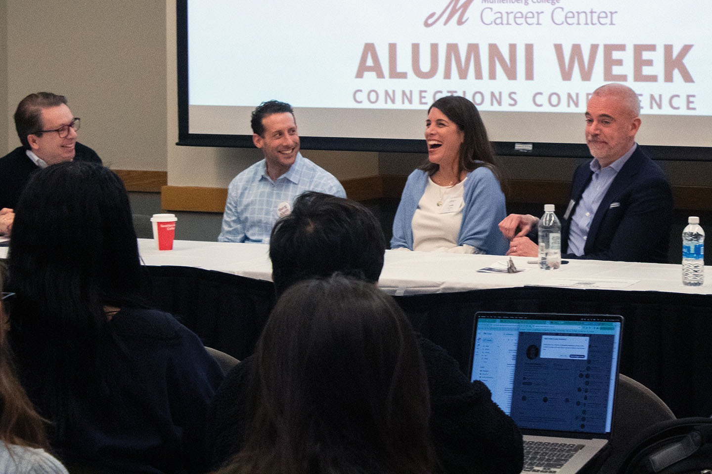 Four people on a panel sit at a table in front of a group of students
