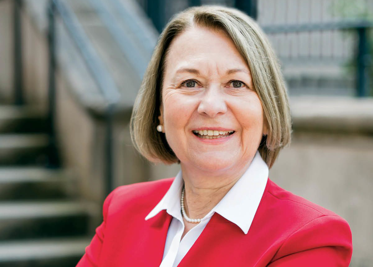 A portrait photo of a woman smiling at the camera in a red suit jacket