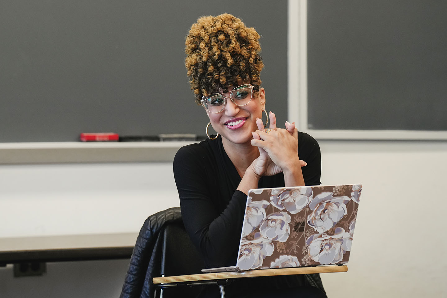A college professor sits in front of her class with a laptop open on the desk in front of her