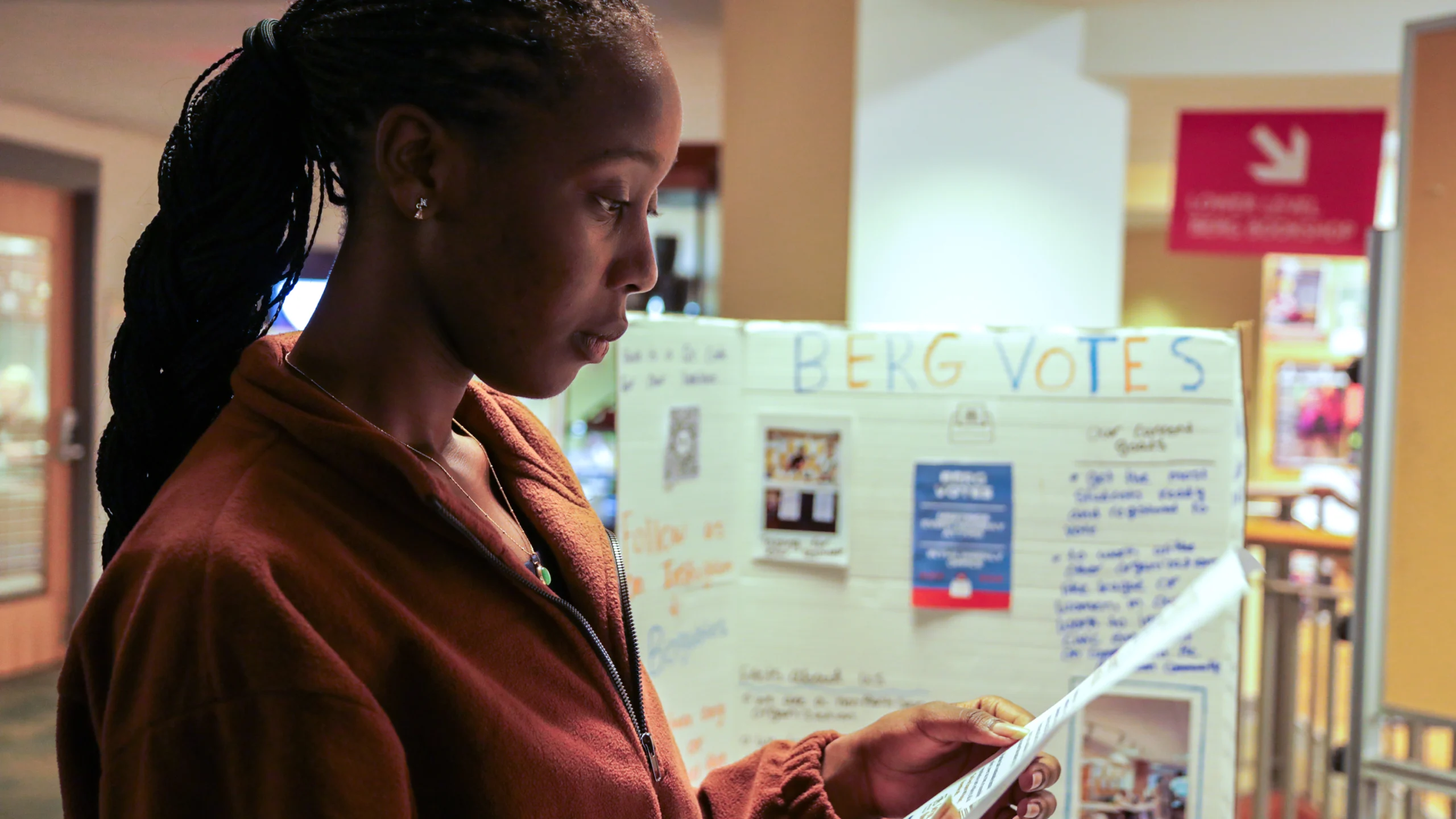 Photo of a student looking at a paper in front of a Berg Votes sign.