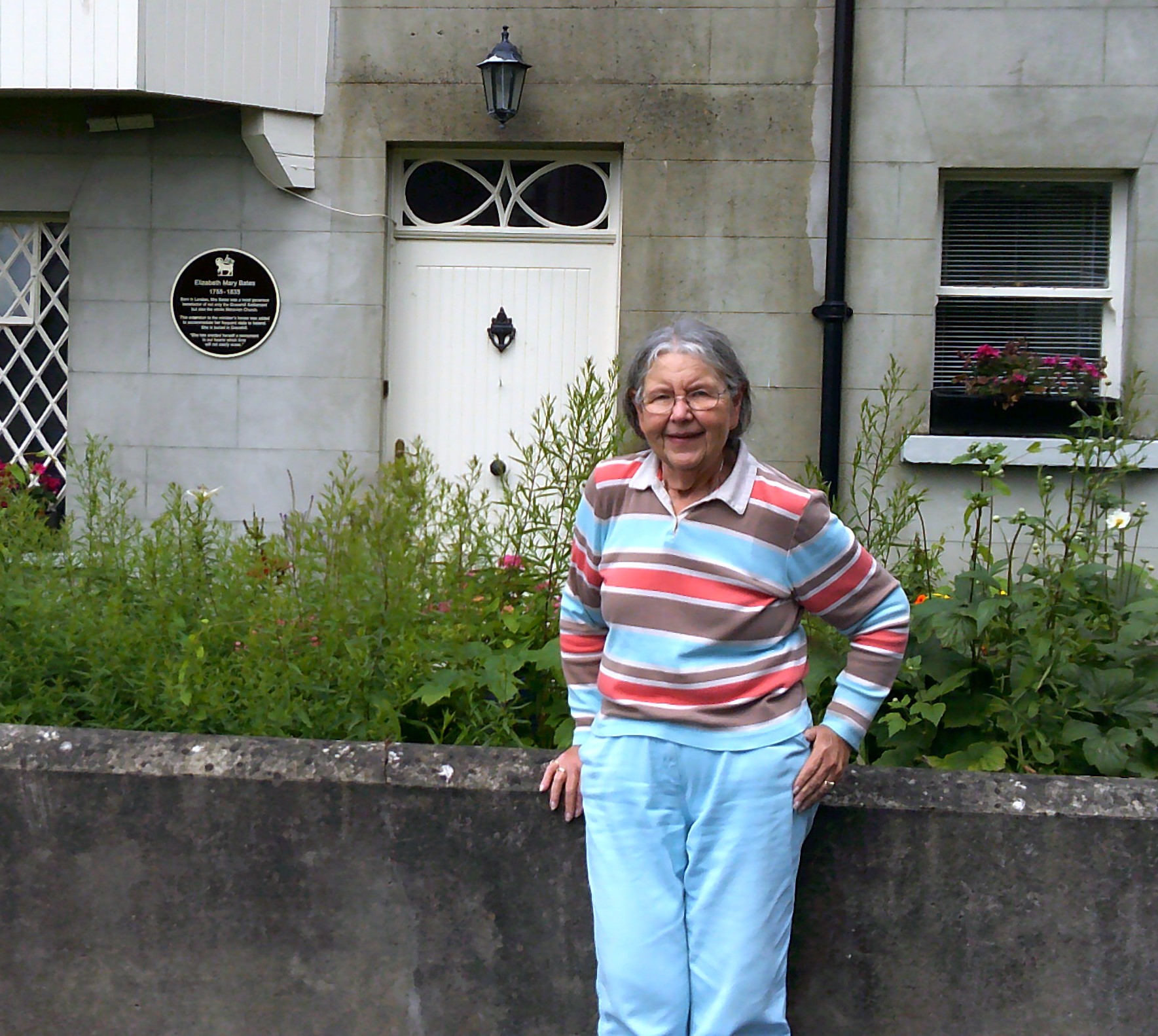 A woman poses for a photo in front of a planter and a white door