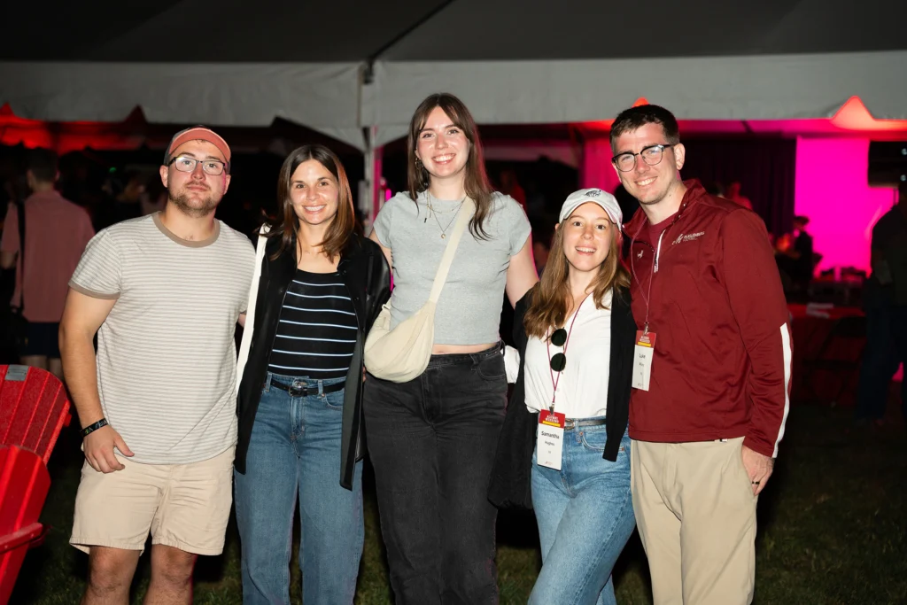 A group of five adults smiles for a photo under a tent