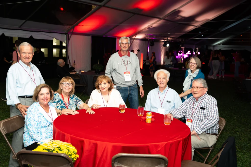 A group of adults sit at a table with a red tablecloth