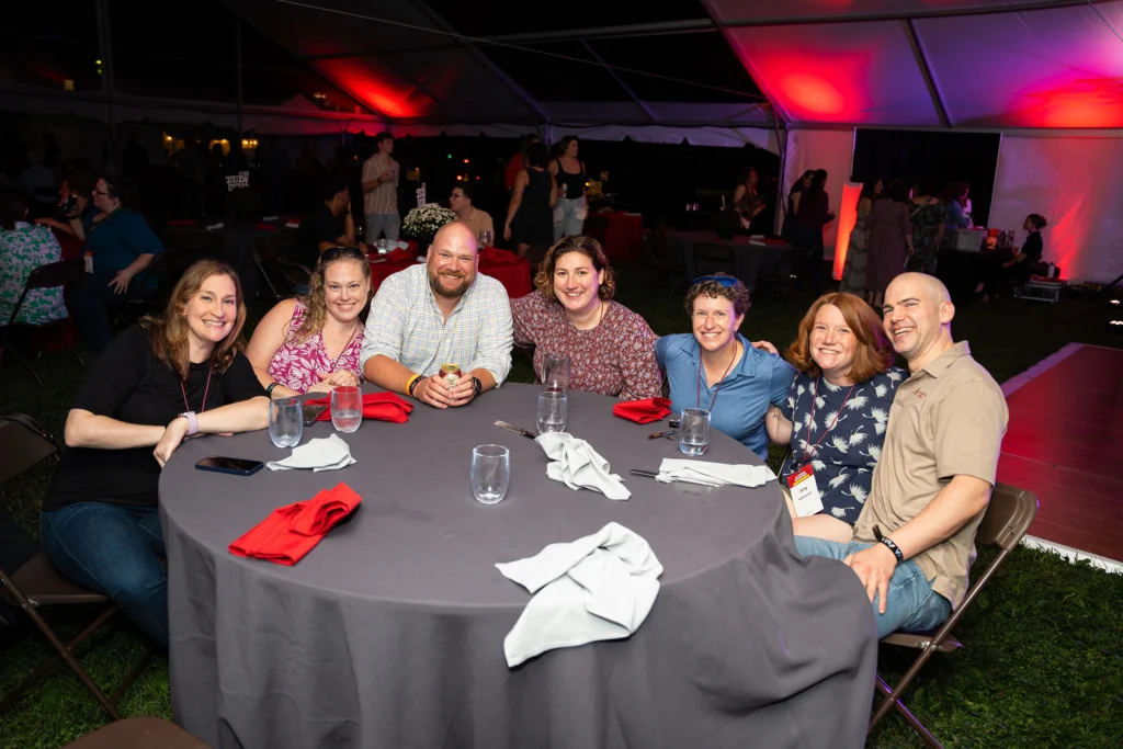 A group of people, seated around a table with a gray tablecloth, smile