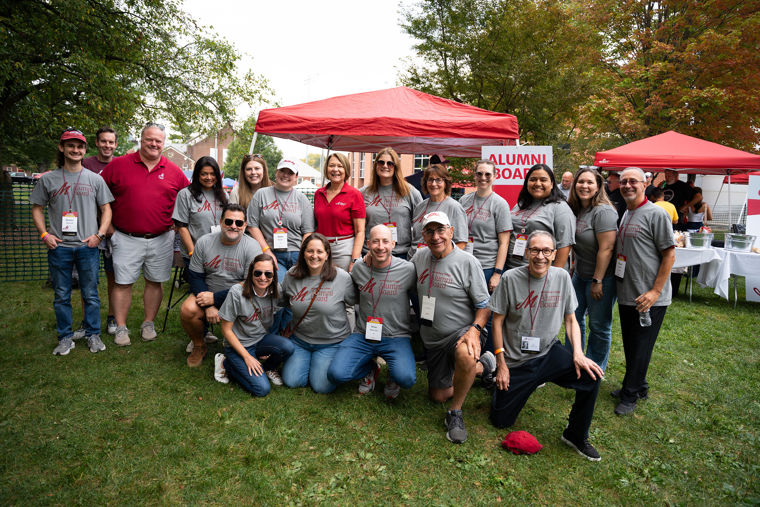 A group of alumni with Muhlenberg's president at a tailgate in front of a tent with a sign reading Alumni Board