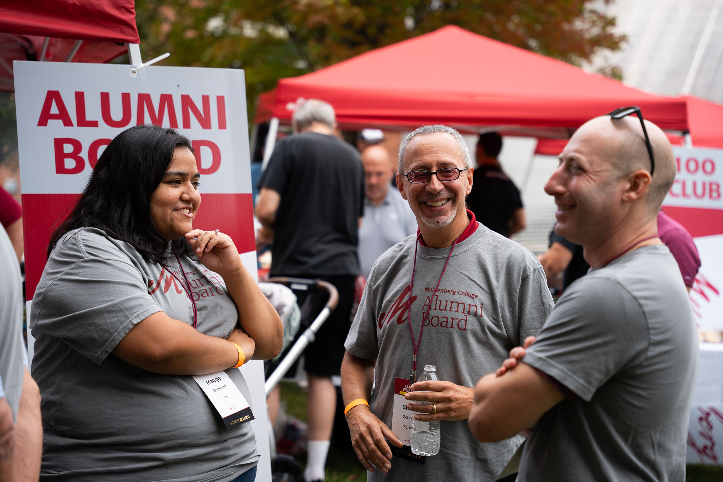 Three people converse in front of a sign that says Alumni Board