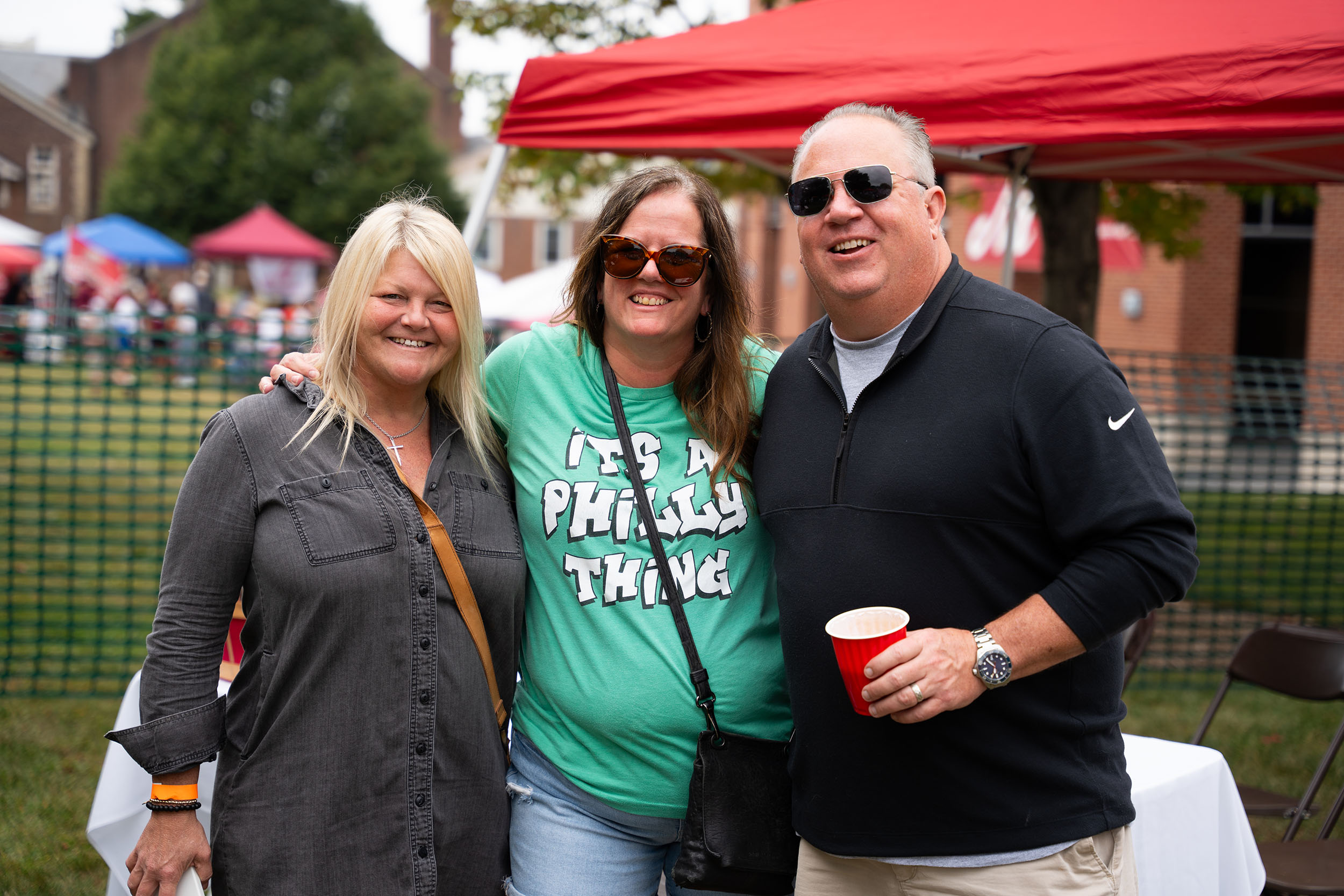 Three smiling people pose for a photo at a tailgate