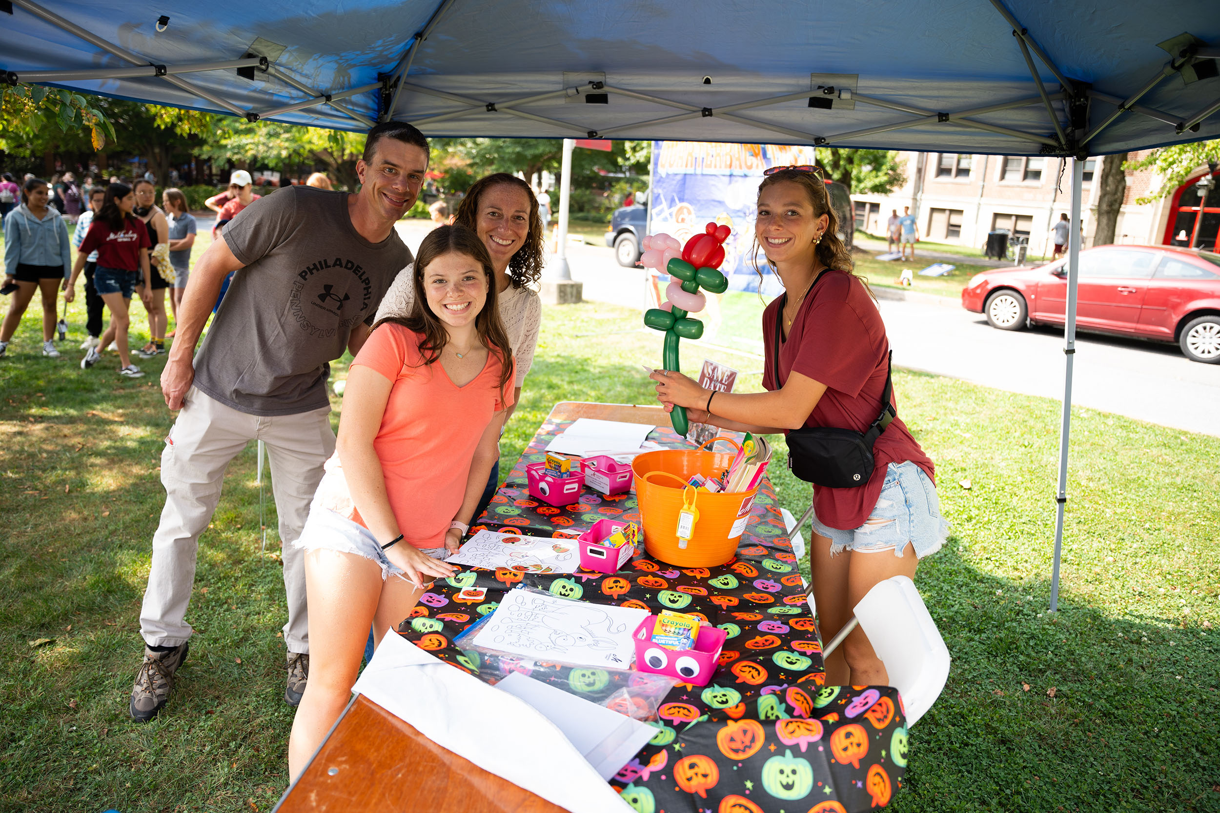 Four people, one holding a balloon animal, pose for a photo under an outdoor tent