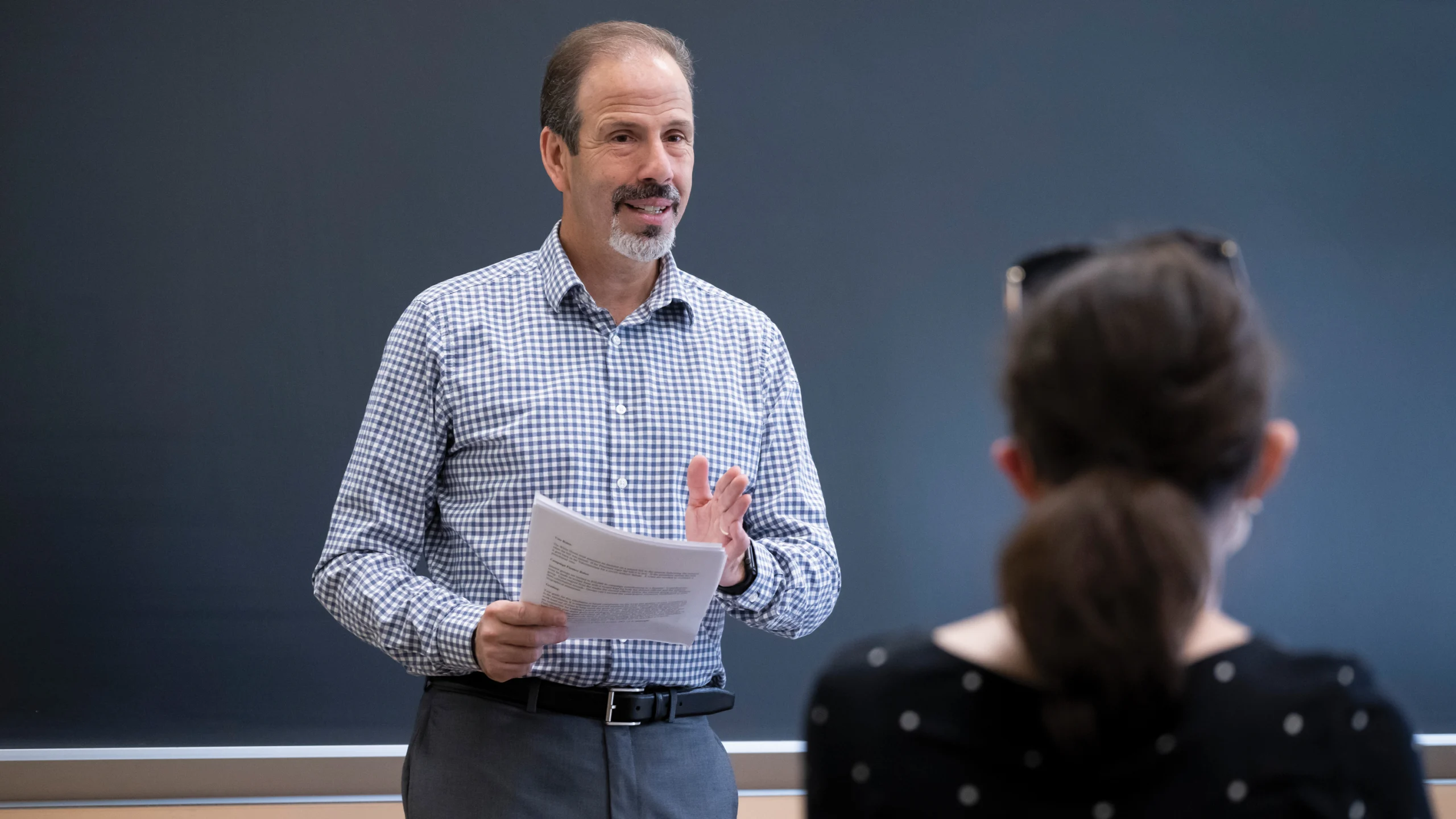 Photo of Christopher Borick teaching in front of a class with a blackboard behind him.