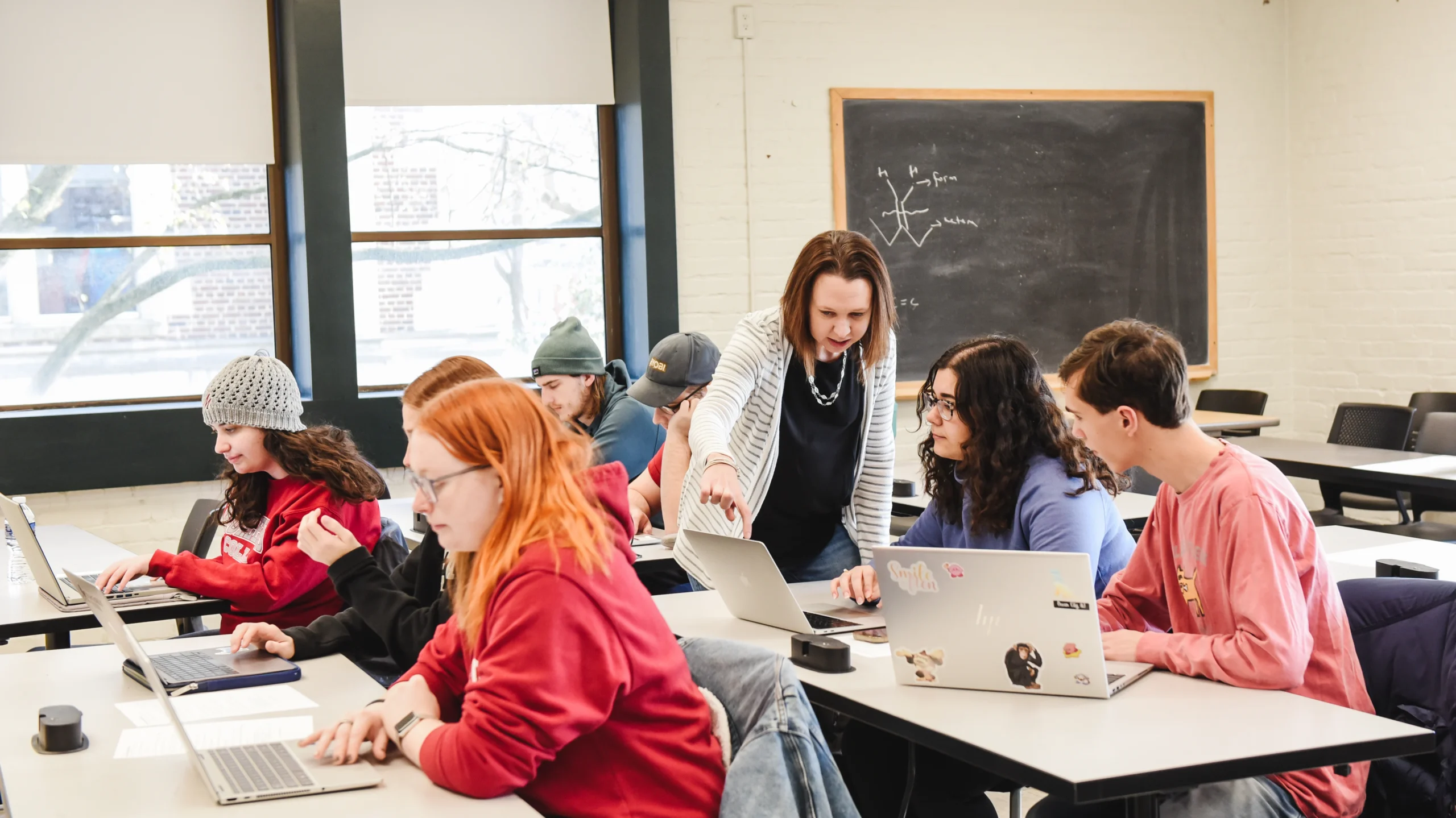 Associate Professor Allison Davidson points to a student's computer screen while other students work around her on computers in the classroom.