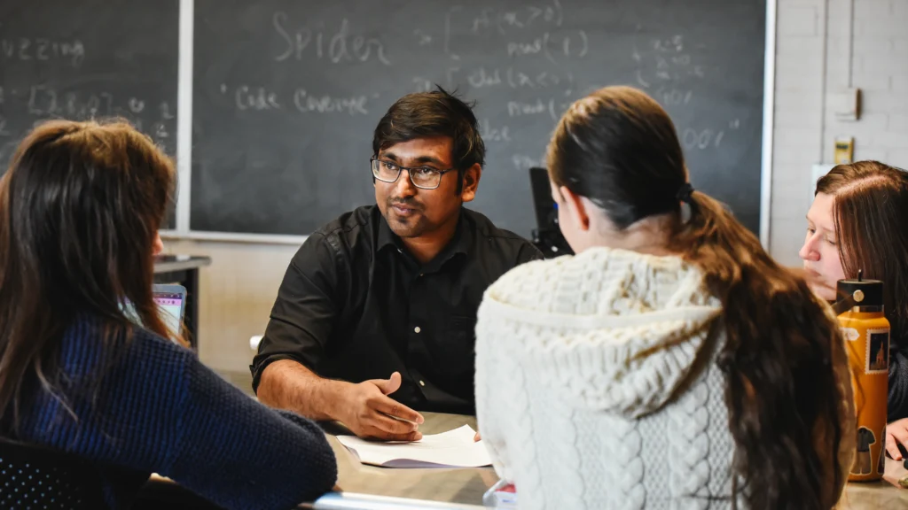 Assistant Professor Proyash Podder faces the camera as he speaks with a group of students in the foreground.