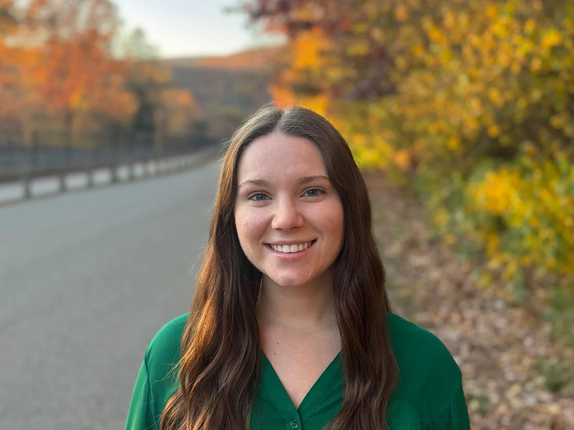 A headshot of a young woman in front of fall foliage