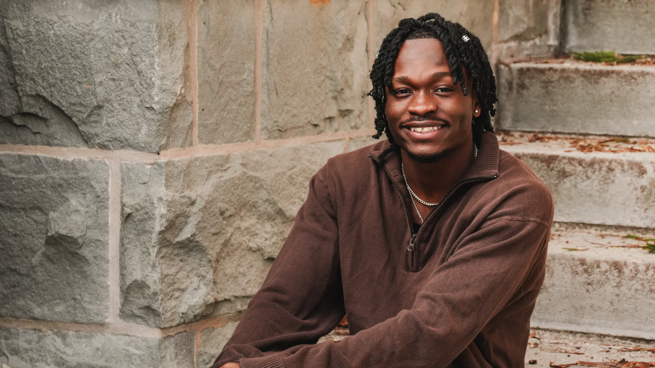 Ibrahim Sidibeh smiling at the camera while seated on stone steps