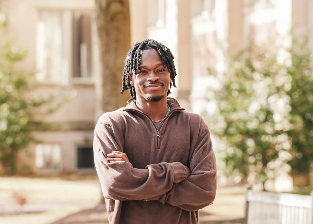 Ibrahim Sidibeh smiling at the camera with his arms crossed outside