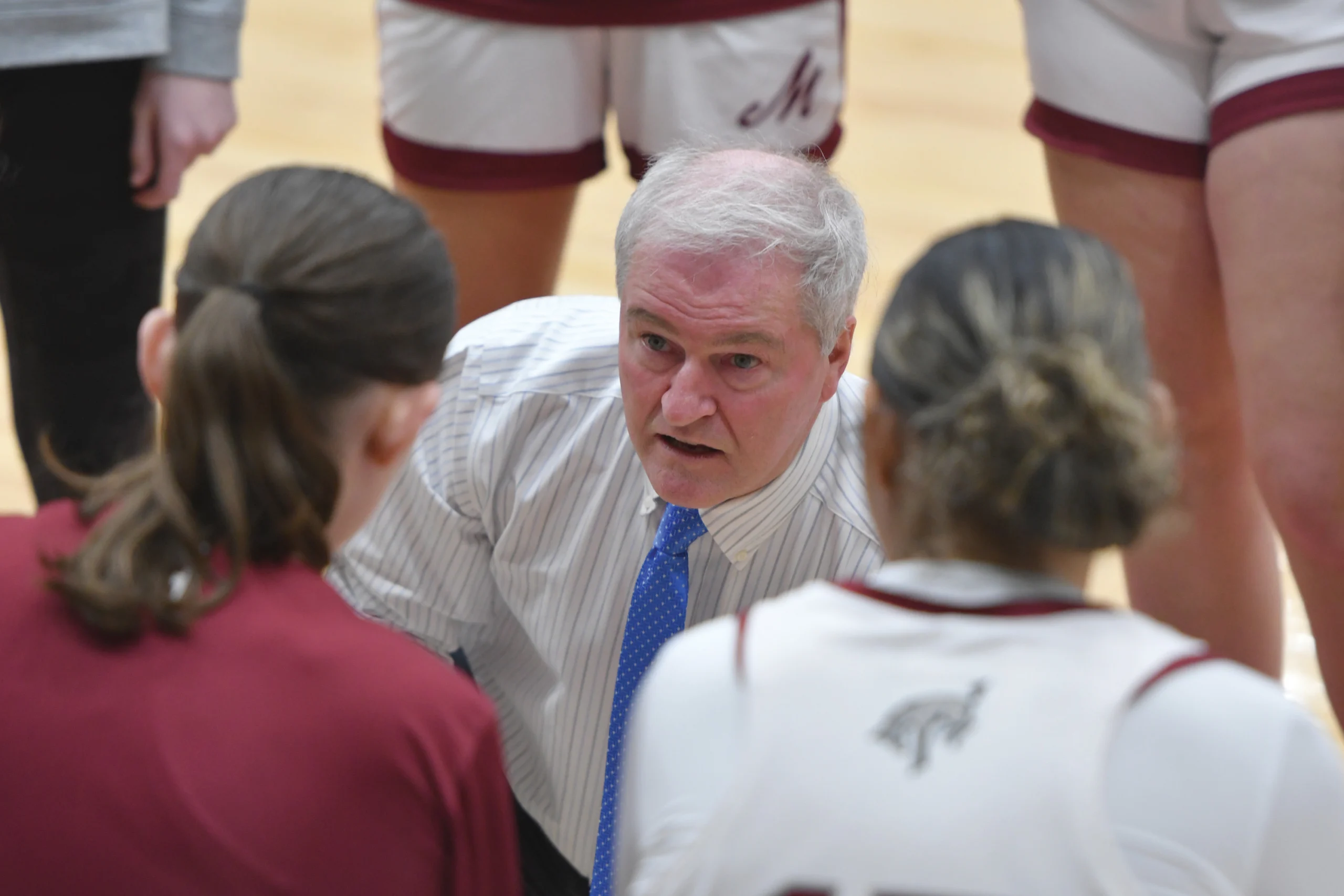 A women's basketball coach speaks to players seated on the bench