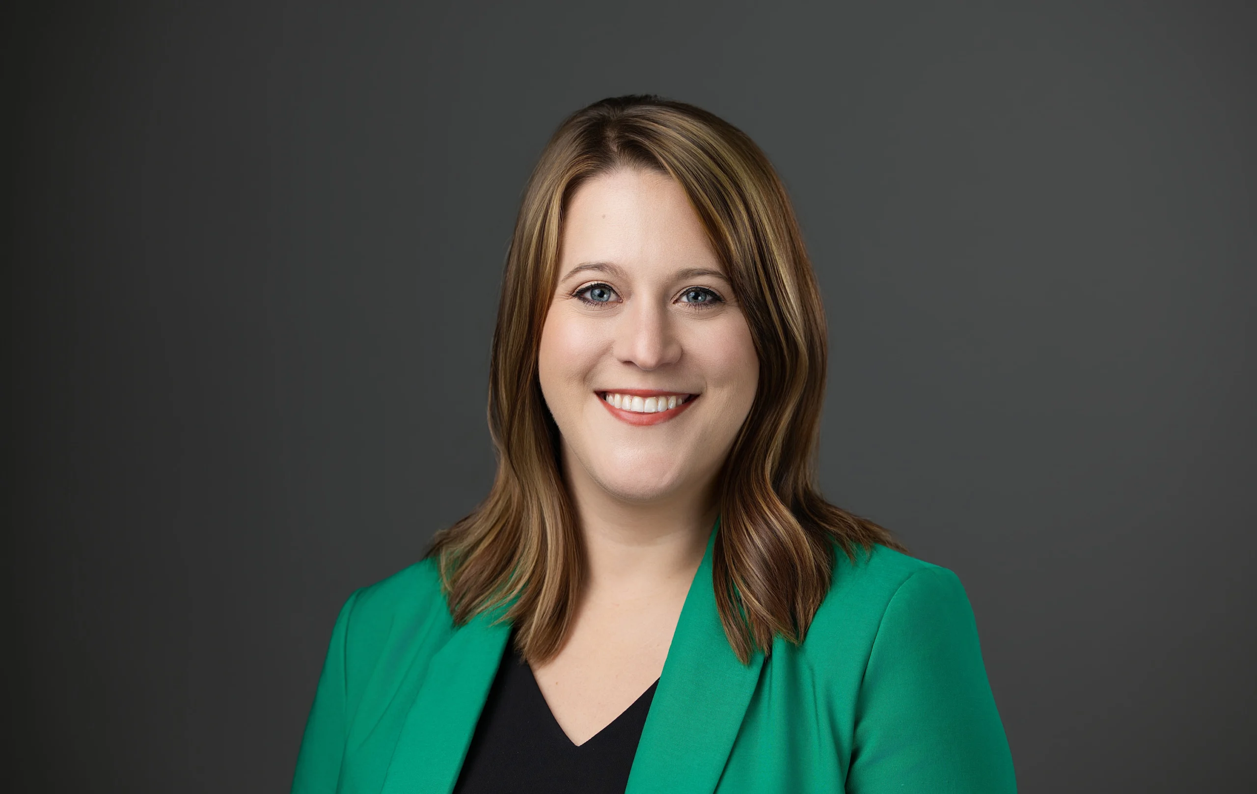 A headshot of a woman with long hair in a green blazer